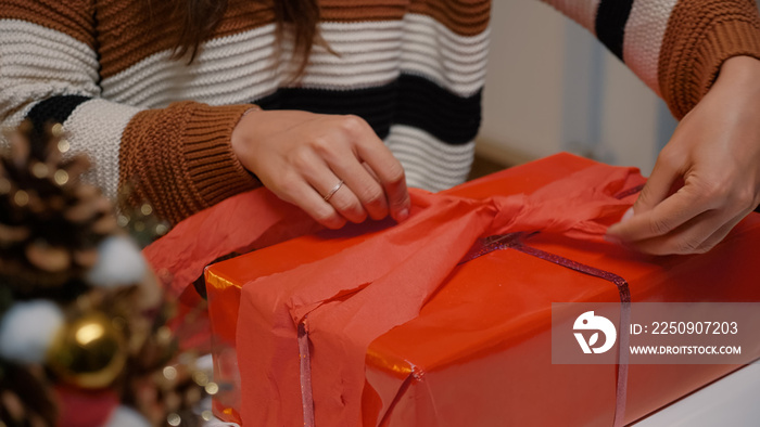 Young adult wrapping gift box in red paper to give to friends at christmas eve celebration party. Wo