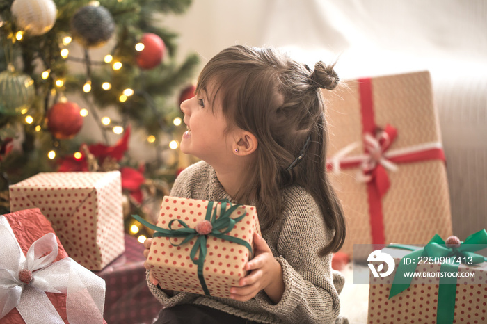 Pretty little girl is holding a gift box and smiling while sitting on her bed in her room at home