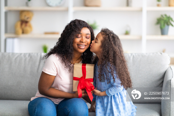 母亲节庆祝活动。可爱的黑人小女孩送给妈妈包装好的节日礼物，并亲吻她。