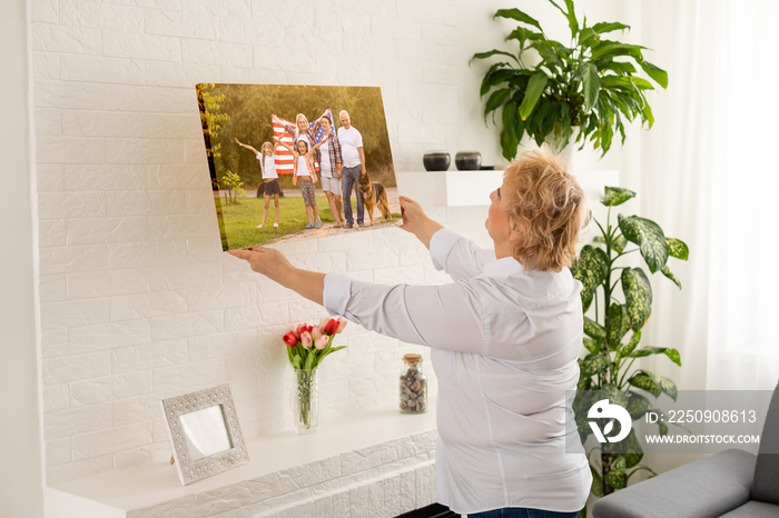 A happy blonde woman is holding a large wall canvas portrait of her family with young children.