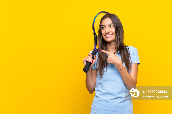 Young tennis player woman over isolated yellow wall pointing to the side to present a product