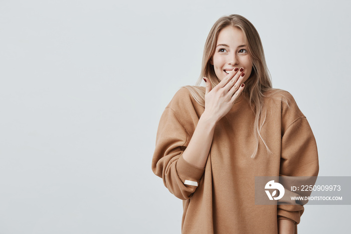 Happy blonde woman closing her mouth with hands going to see surprise prepared by husband standing a