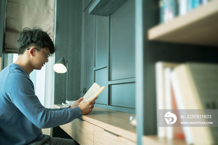 Male Asian reading a book in bedroom..