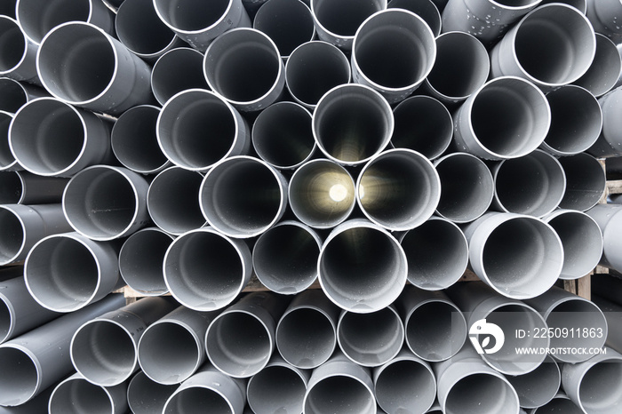 Gray PVC tubes plastic pipes stacked in rows with light shinning through