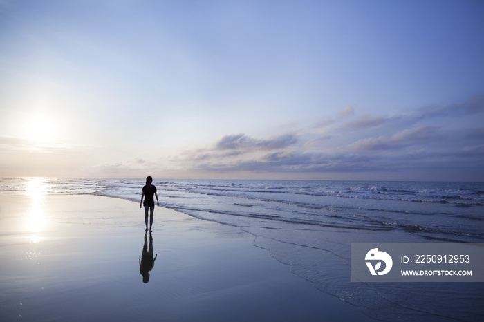 Woman walking on beach at sunrise