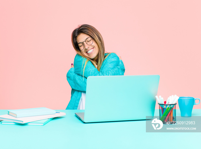 young pretty woman working with a laptop feeling in love, smiling, cuddling and hugging self, stayin