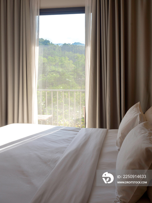 Close up empty clean bed with two pillows near the glass door and curtain with warm morning sunlight