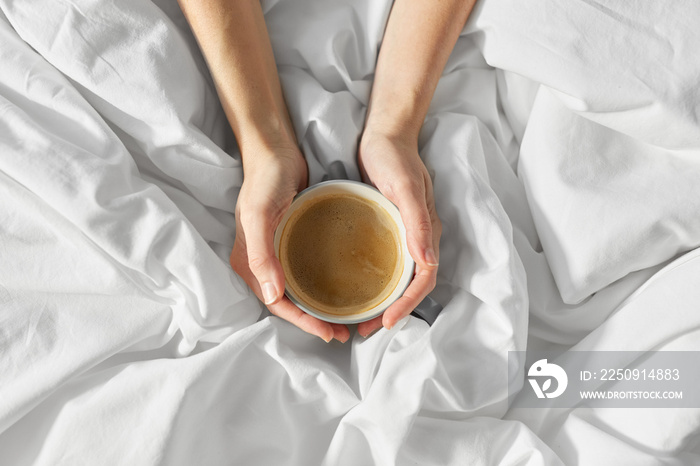 morning, drink and people concept - hands of young woman with cup of coffee in bed at home bedroom