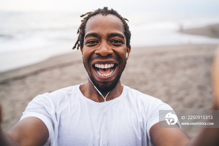 Laughing black man holding camera and taking selfie on seacoast