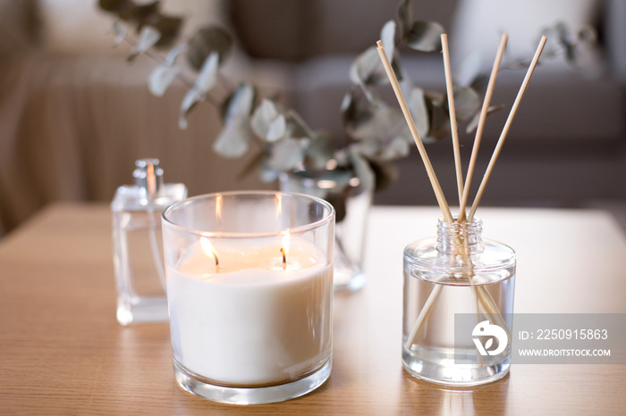 decoration, hygge and aromatherapy concept - aroma reed diffuser, burning candle and perfume on tabl