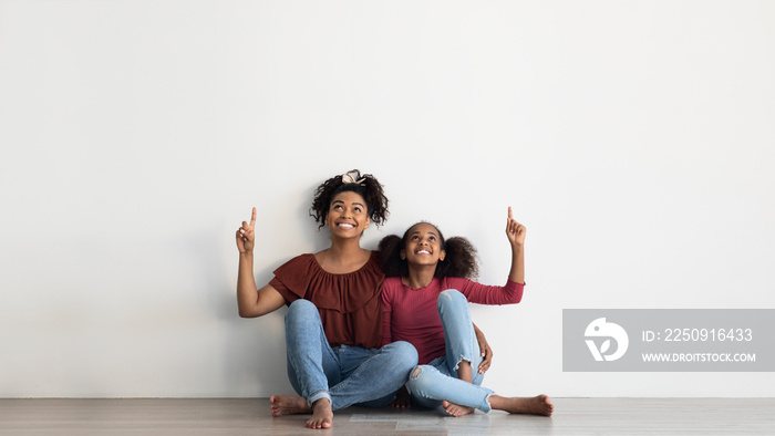 Beautiful afro american mother and daughter pointing up, copy space