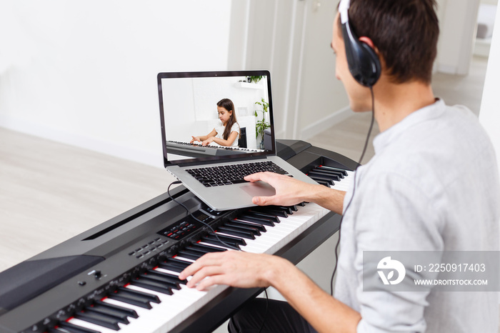A man learning to play piano online with a computer staying at home. Concepts of self taught, stayin