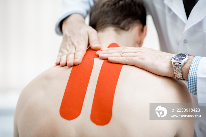 Senior therapist applying kinesio tape on a mans neck during the medical treatment in the office