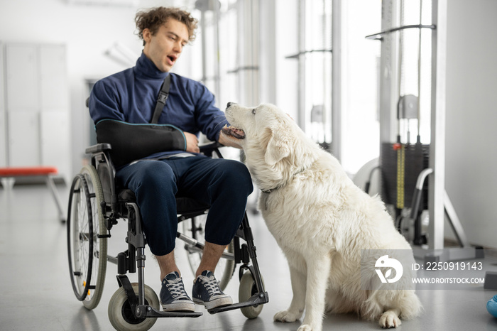 在康复中心，一个残疾的年轻人和他友好的狗坐在轮椅上。Con