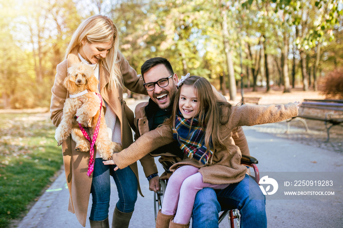 残疾父亲坐在轮椅上，与女儿和妻子在公园户外玩耍。