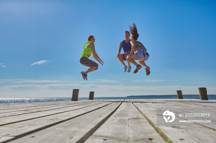 Friends on pier jumping in mid air