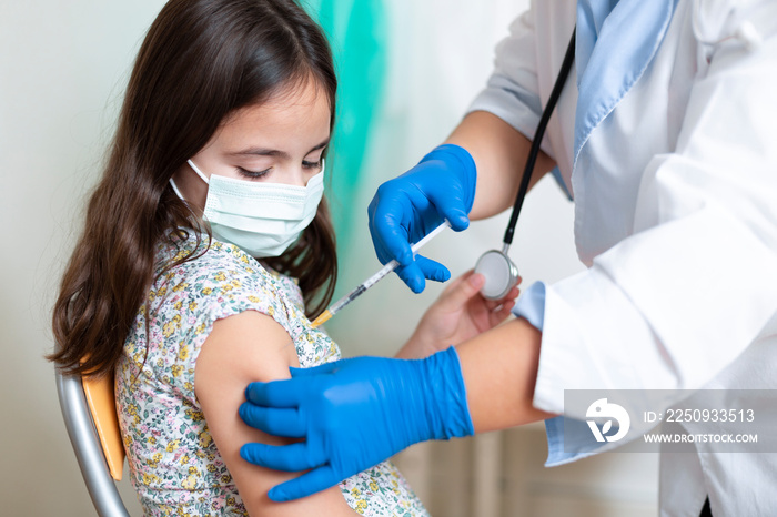 戴着口罩的高加索小女孩看着医护人员为她接种疫苗。儿童疫苗