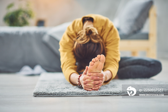 Caucasian brunette stretching leg while sitting on the rug in bedroom.