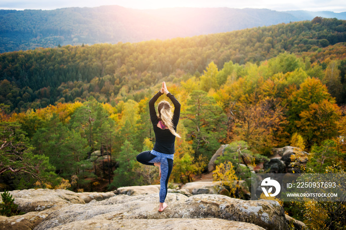 迷人的年轻女性正在高高的岩石上练习瑜伽和瑜伽体式