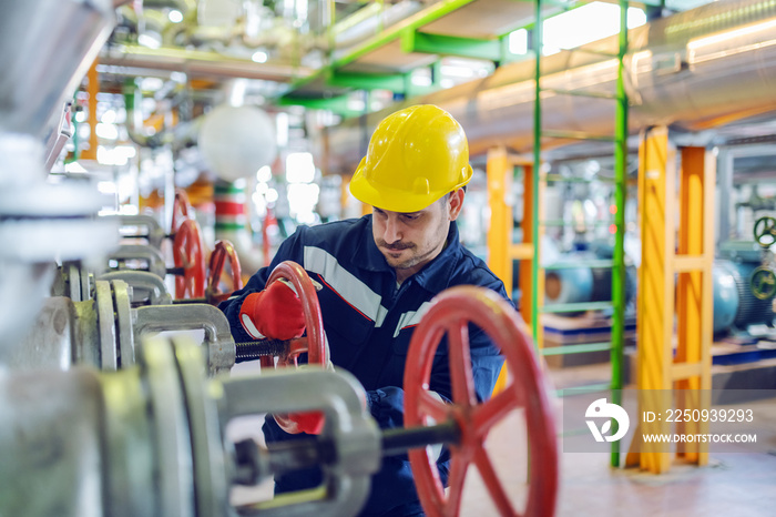 Hardworking handsome caucasian plant worker in protective suit and with helmet on head trying to scr