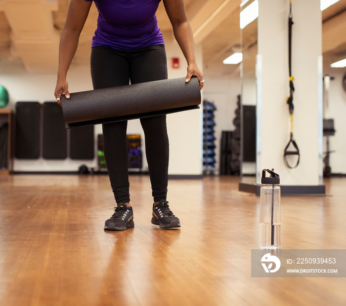 Low section of female athletes placing exercise mats on hardwood floor in yoga class