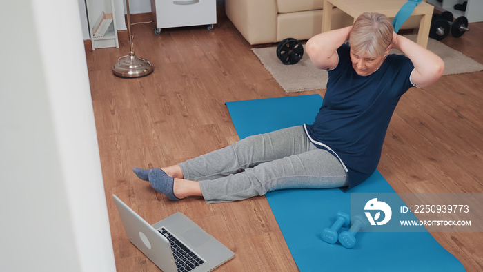 运动型老年妇女在瑜伽垫上锻炼，看在线健身计划。老年养老金领取者