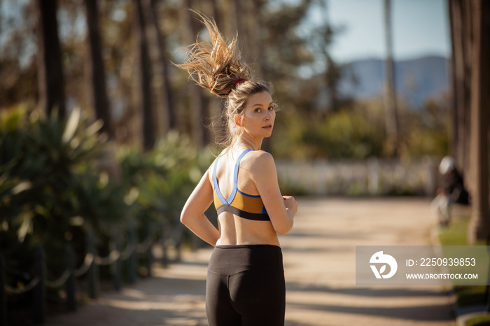 Rear view portrait of confident sportswoman wearing sports clothing while jogging on footpath in par