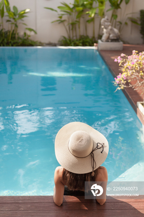 back view of young woman in swimsuit and hat sitting in pool of hotel