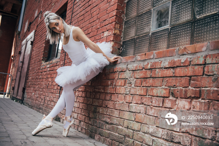 美丽的年轻芭蕾舞演员靠在砖墙旁，目光移开