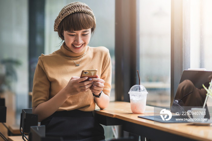 Young asian woman enjoying playing on their phone and laptop  at café.