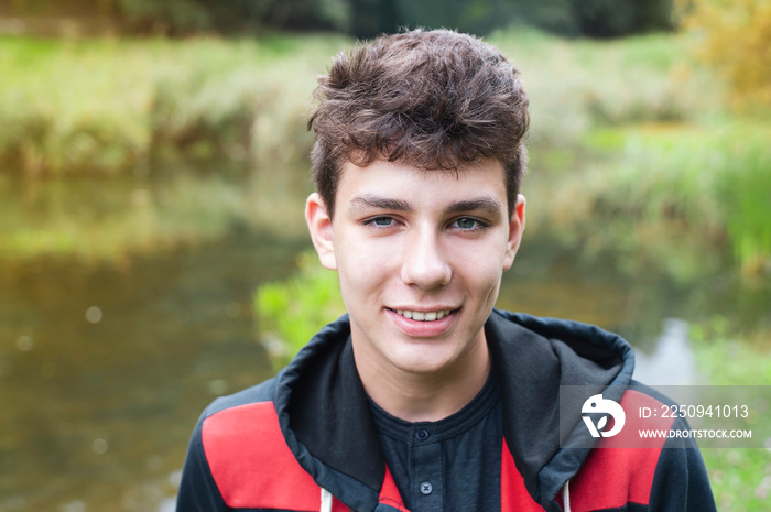 A young man in a sports suit after a jog by the lake rests and smiles, he has healthy, beautiful tee