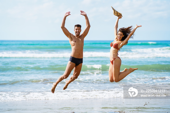 Funny young couple with beautiful bodies jumping on a tropical beach.