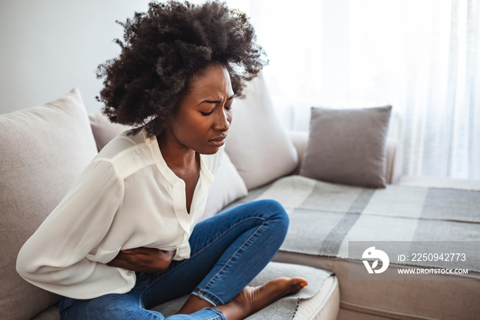 Sad beautiful woman sitting on the couch and feeling spasm and symptoms of pms. Shot of a young woma