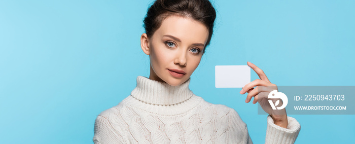 Brunette model in knitted sweater holding blank card isolated on blue, banner.