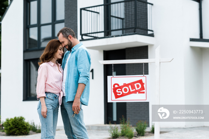 happy man and woman with closed eyes standing near house