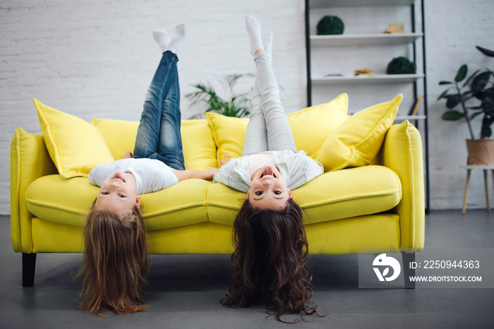 Funny young teenagers lying on yellow sofa and looking straigt on camera. They smile. Girls hold leg