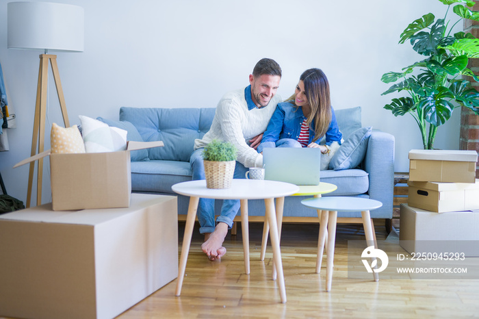 Young beautiful couple sitting on the sofa drinking cup of coffee using laptop at new home around ca