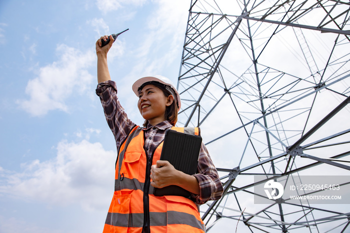 Electrical Asian beautiful engineer with high voltage electricity pylon and using walkie talkie and 