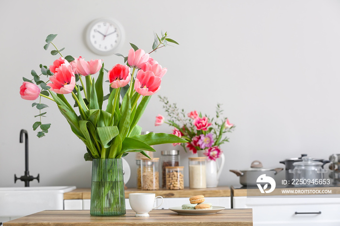 Vase with beautiful tulips, cup and macarons on table in light kitchen