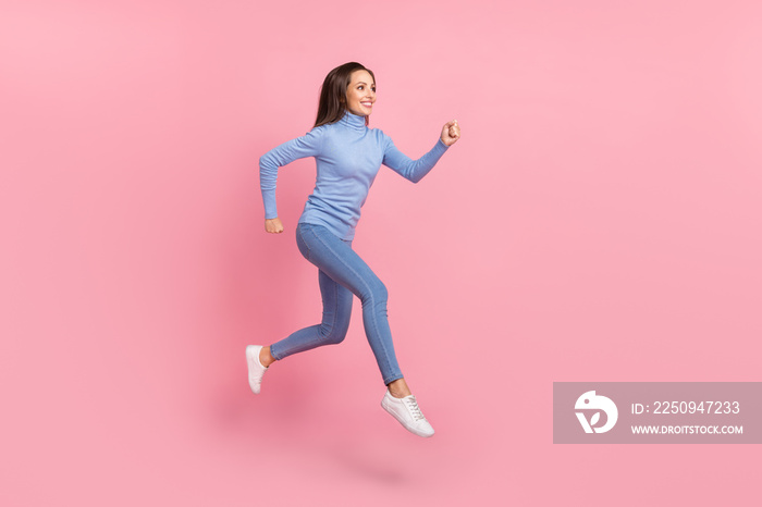 活泼开朗的女士的侧面照片，在空旷的地方跳跃奔跑，穿着蓝色高领牛仔裤和运动鞋。