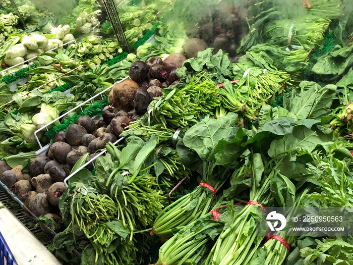 Assorted green leafy vegetables and root crops at the fresh produce section in a grocery store.