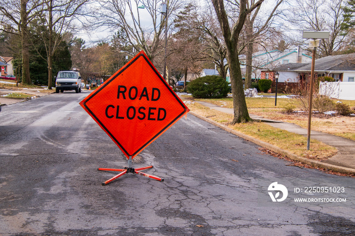 Orange diamond shaped road closure sign on road in a neighborhood near a house.