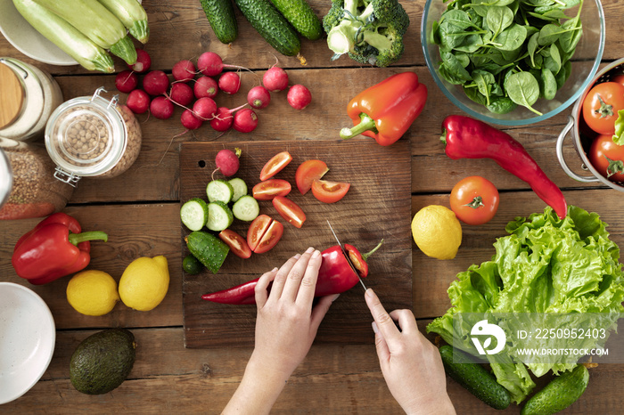 一套新鲜蔬菜，用于烹饪健康的夏季食物，木质背景俯视图。女性双手