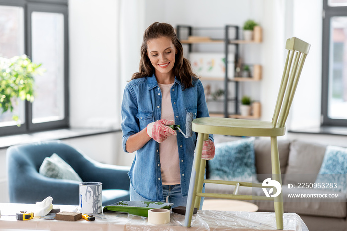 renovation, diy and home improvement concept - happy smiling woman in gloves with paint roller paint