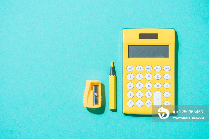 top view of arrangement of calculator, pencil and pencil sharpener on blue backdrop