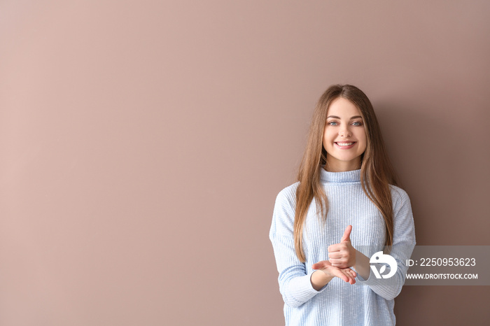 Young deaf mute woman using sign language on color background