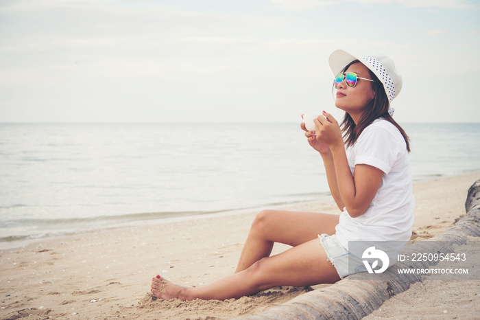 Beautiful young woman with coffee in hands sitting on the beach