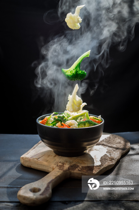 蔬菜的蒸汽胡萝卜西兰花花椰菜放在黑色碗里，一个热气腾腾的。滚烫的Hea