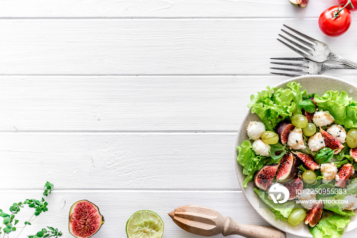 Salad with figs, mozzarella and grapes on a white wooden background.