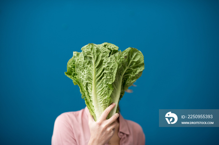 Portrait of a young woman with green lettuce on the blue wall background